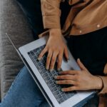 pexels-photo-6893955-6893955 A person typing on a laptop while seated on a couch with casual attire, perfect for remote work imagery.